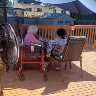 Two people sitting on a deck under a large umbrella, enjoying a sunny day.