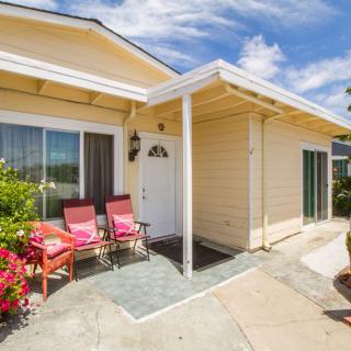 A sunny view of a house exterior with a cozy front porch featuring two red chairs and surrounding greenery.