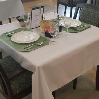 A neatly set dining table in a restaurant, with white plates and green placemats.