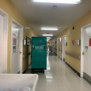 A view of a hospital corridor featuring a cleaning cart and patient rooms.