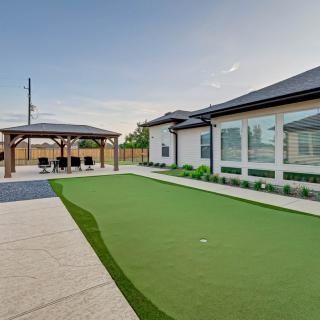A modern backyard with a putting green, patio, and pergola adjacent to a house.