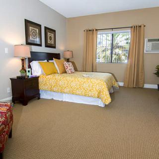 A cozy bedroom with a neatly made bed, soft lighting from table lamps, and a view out the window.