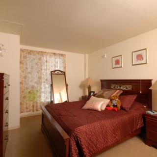 A cozy bedroom with a neatly made bed, standing mirror, and decorative elements.