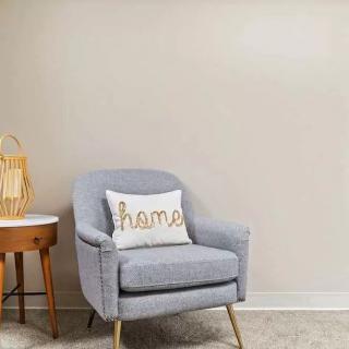 A cozy living room corner with a gray armchair and a 'home' cushion next to a wooden side table.