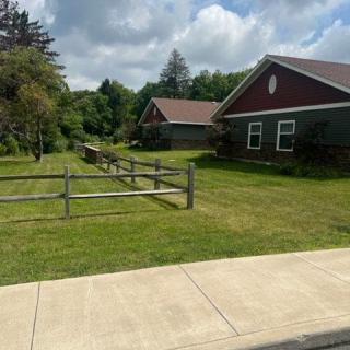 A peaceful suburban scene with houses, a wooden fence, and a neatly maintained lawn under a partly cloudy sky.