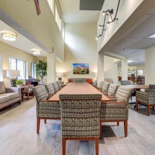 A spacious, modern dining room with a long table and upholstered chairs, illuminated by ceiling lights.