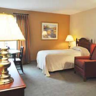 A cozy hotel room featuring a bed, armchair, and warm lighting.