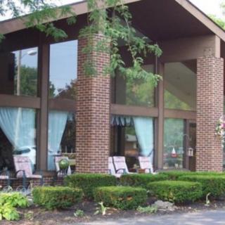 A modern building with large windows, featuring outdoor chairs and surrounded by plants and trees.