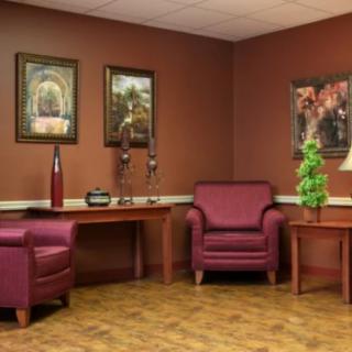 A cozy office waiting area with upholstered chairs, artwork on the walls, and decorative items.