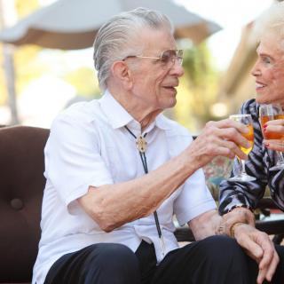 An elderly couple enjoying drinks and having a conversation outdoors.
