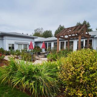 A cozy house with a lush garden and patio area featuring red umbrellas and a wooden pergola.
