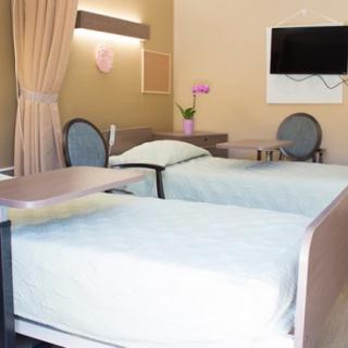 A clean and well-organized hospital room with two beds, a TV, and seating area.