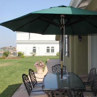 A cozy patio setup with a glass table, chairs, and a large green umbrella in a backyard.
