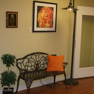 A cozy corner with a decorative bench, an orange pillow, wall art, and a standing lamp.