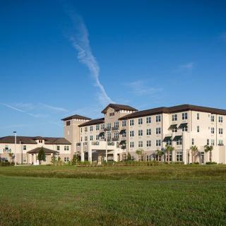 A modern hotel building surrounded by greenery under a clear blue sky.