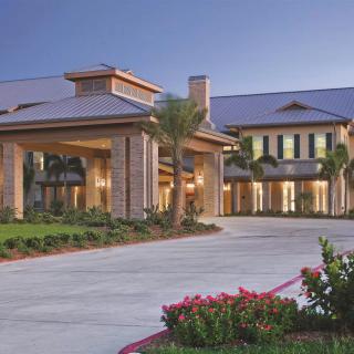 A large, well-lit building with an inviting entrance and surrounding palm trees in the evening.