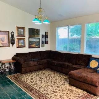 A cozy living room featuring a brown sectional sofa, decorated with wall art and an area rug on green tile flooring.