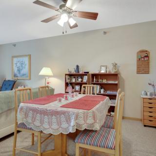 A cozy dining area with a table set for four, surrounded by wooden furniture and lit by a ceiling fan.