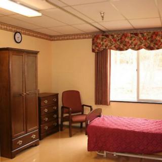 A simple bedroom with a bed, wardrobe, and chair.
