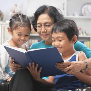 A grandmother reads a book with her two grandchildren, sharing a moment of learning and togetherness.