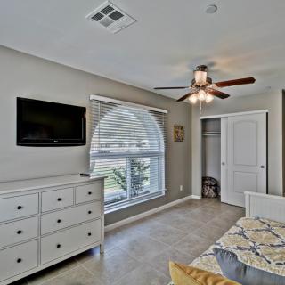 A modern bedroom with a dresser, bed, ceiling fan, and flat-screen TV.