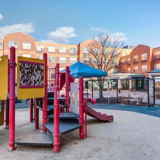 A colorful playground with a slide and various equipment in an urban park setting on a sunny day.