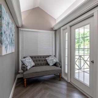 A cozy corner with a small sofa and decorative pillows near large windows and glass doors.