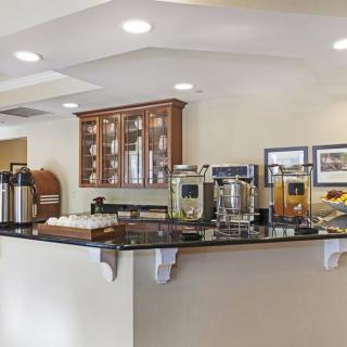 A hotel breakfast area featuring a self-serve buffet with coffee and juice dispensers.