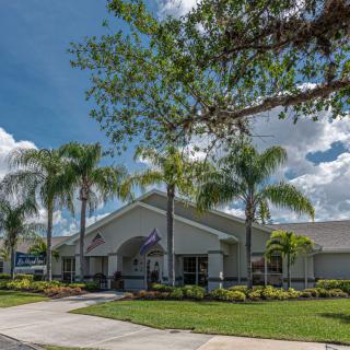 A residential building surrounded by palm trees and lush landscaping under a sunny sky.