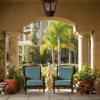 A cozy patio area with two chairs surrounded by potted plants and palm trees, framed by architectural columns.