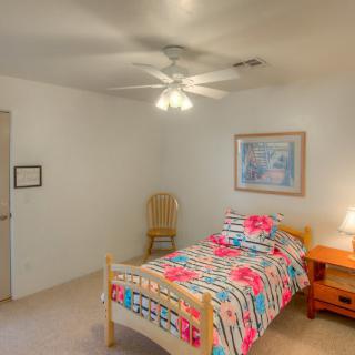 A cozy bedroom featuring a single bed with colorful bedding, a wooden nightstand with a lamp, and a ceiling fan overhead.