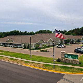 A large building with an American flag in front, adjacent to a parking lot and a road.