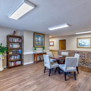 A cozy interior space features a bookshelf, table with chairs, and artwork on the walls.
