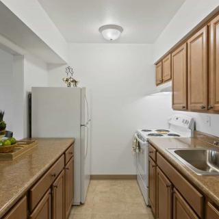 A compact kitchen in an apartment with wooden cabinets and white appliances.