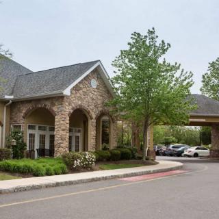 A modern building with a stone facade and an entrance surrounded by trees and a parking area.