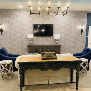 A stylish living room with blue chairs, a chandelier, and a television mounted on a wallpapered wall.