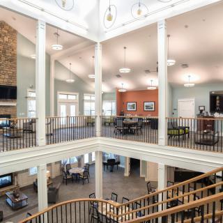 A spacious and modern atrium with a central staircase and upper balcony, featuring comfortable seating areas and elegant lighting fixtures.