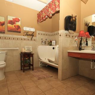 A warmly decorated bathroom featuring a bathtub, toilet, and sink with a tiled floor and wall art.