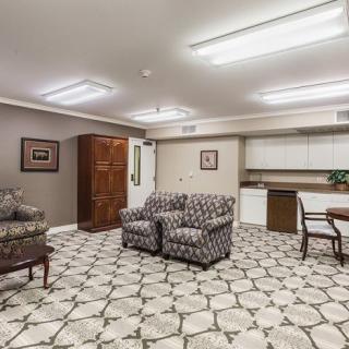 A modern living space with a patterned carpet, comfortable seating, and a kitchenette.