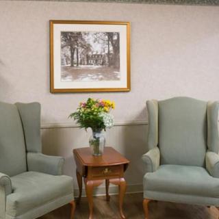 A cozy seating area with two armchairs, a small wooden table with a vase of flowers, and a framed painting on the wall.