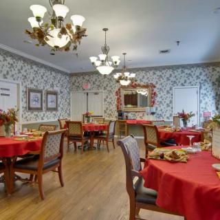 A cozy dining room with red tablecloths, decorative chandeliers, and floral wallpaper.