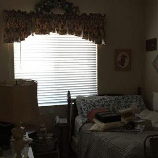 A cozy bedroom with a bed, lamp, and window with blinds.