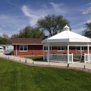 A serene view of a house with a red roof, complemented by a white gazebo in the yard under a clear blue sky.