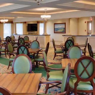A spacious and elegantly designed restaurant dining area featuring wooden tables, green cushioned chairs, and chandeliers.