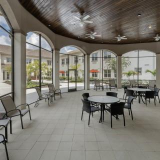 A bright indoor patio area with tables and chairs, surrounded by large arched windows.