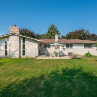 A sunny backyard view of a single-story house with a patio and lawn.