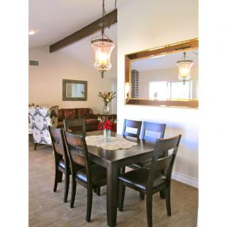 A cozy dining room with a wooden table and chairs, accented by a hanging light fixture and a large mirror on the wall.