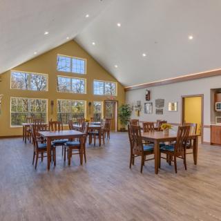A spacious dining area with wooden tables and chairs, large windows, and a high ceiling.