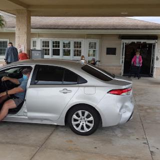 A person is getting into a silver car parked at the entrance of a building.