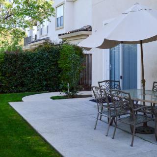 A peaceful backyard patio with a table and chairs under an umbrella, surrounded by greenery.